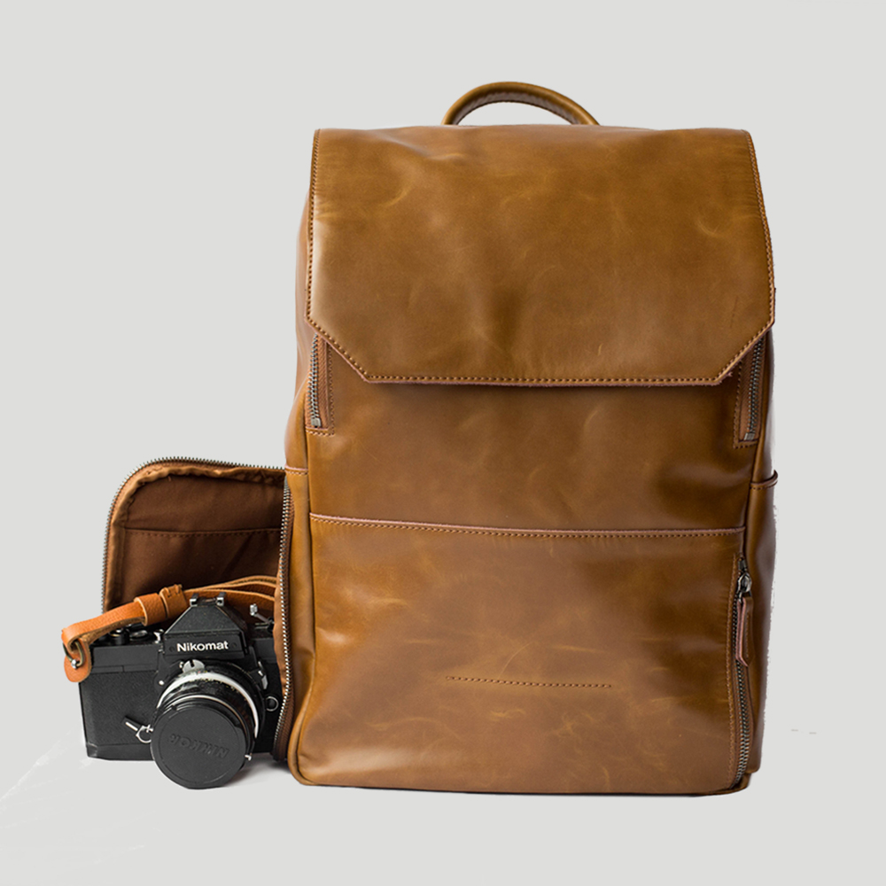 A tan leather backpack with an open pocket exposing a high-quality camera