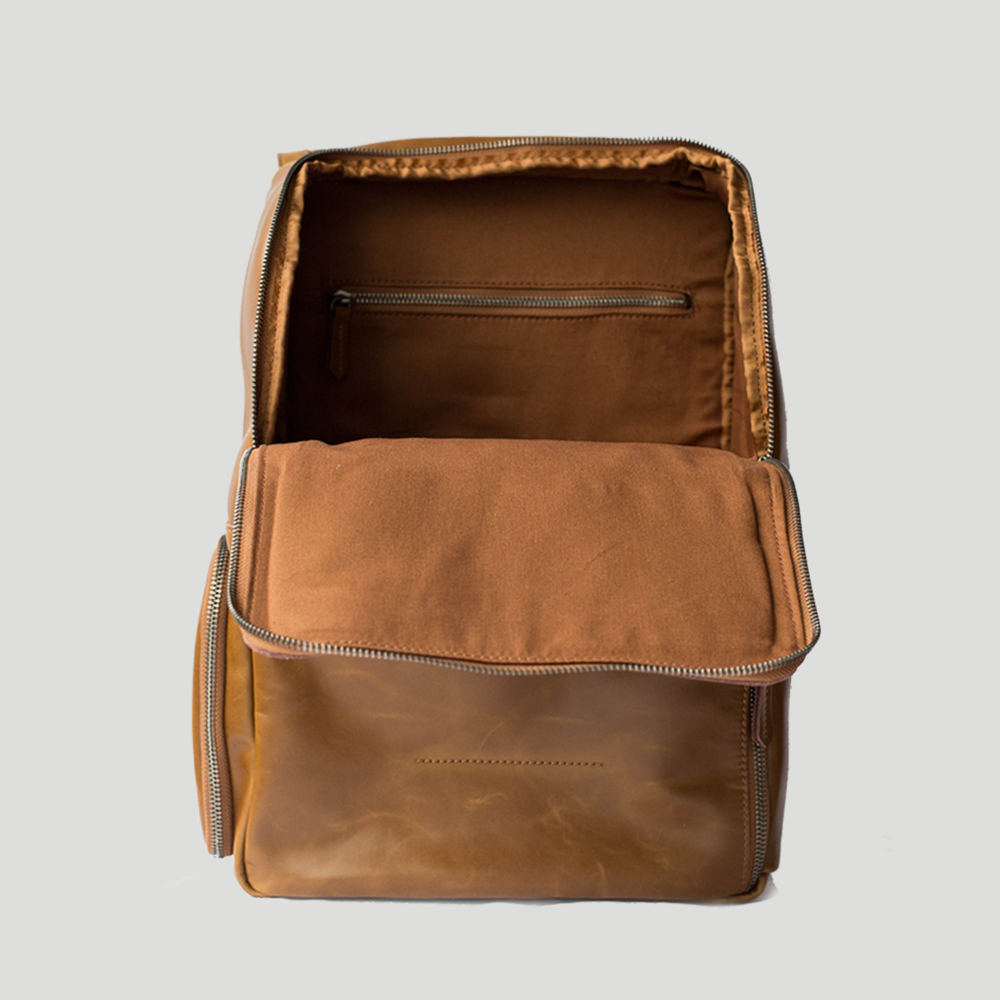 A caramel-colored work backpack with its flap open to display the internal pockets and lining