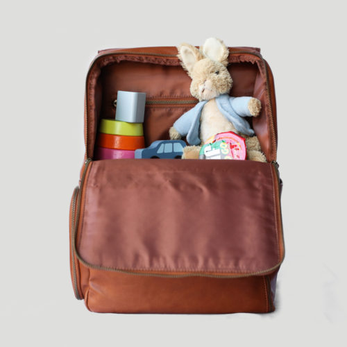An open brown diaper bag backpack exposing a stuffed animal and colorful baby toys inside